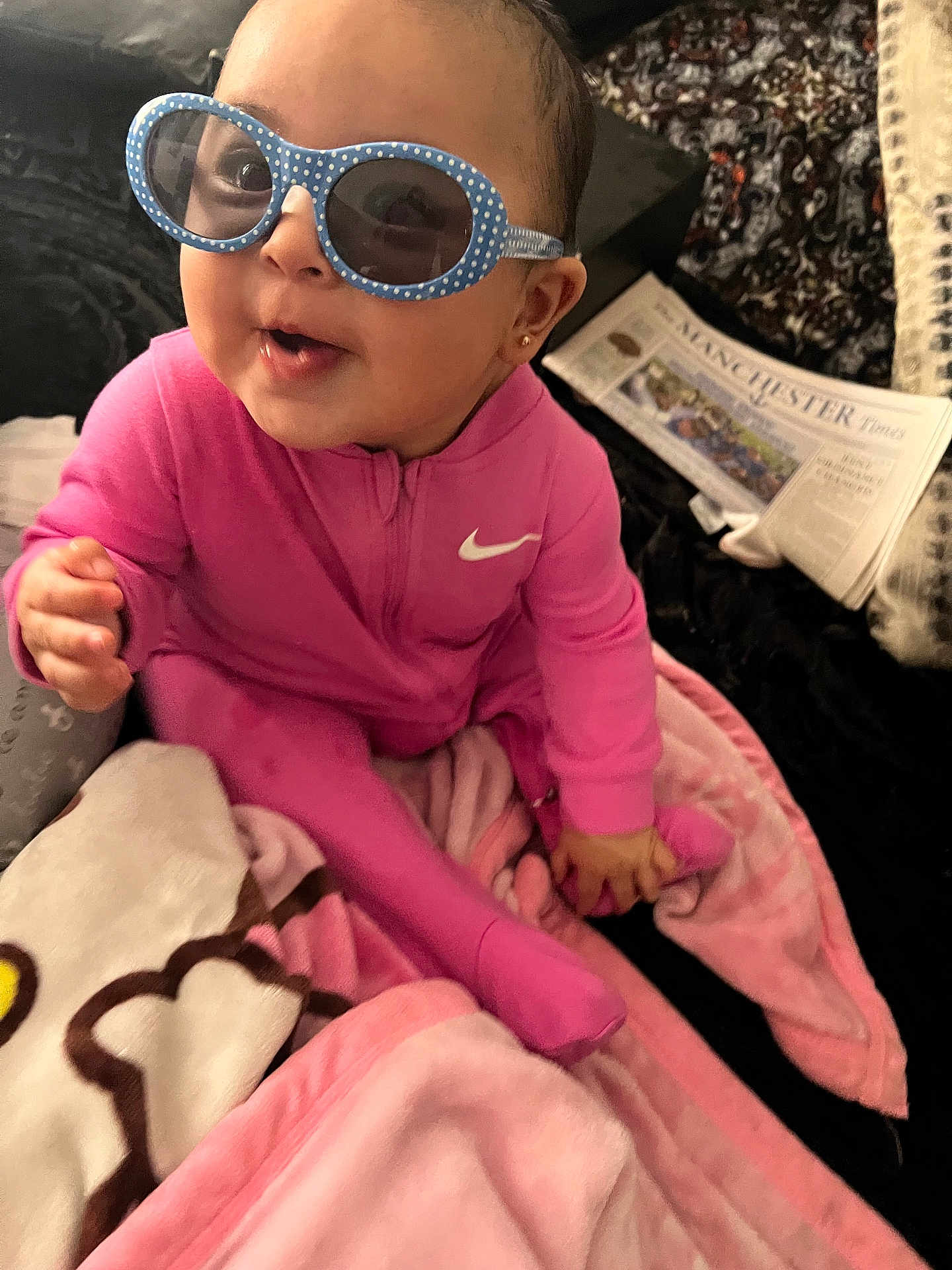 Sarah joined the competition — help win amazing prizes! baby, child, pink_clothing, sunglasses, indoor, blanket, happy, smiling, person, face, head, seated, toy, cozy, nike_logo, polka_dots, newspaper, floor, cute, portrait
