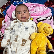 Sarah is registered to the contest to win money with this photo: baby, child, teddy_bear, plush_toy, blanket, bedspread, onesie, sleepwear, cute, smiling, indoors, portrait, child_boy, soft_texture, cozy, lying_down, comfort, toy, expression, warm