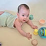 baby, infant, tummy_time, toy, colorful, play, child, cute, indoor, floor, green_outfit, plastic_cups, ball, smile, curious, young_child, skin, hand, face, eyes