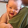 baby, child, smile, face, person, arm, hand, green_shirt, indoor, happy, cute, skin, head, holding, infant, closeup, portrait, young, human, expression
