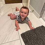 Henry joined the competition — help win amazing prizes! baby, child, crawling, floor, tile, bath_mat, diaper, onesie, smiling, happy, indoor, doorway, wood_floor, curly_hair, skin, hand, foot, head, wall, baseboard