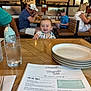 Henry is registered to the contest to win money with this photo: baby, child, restaurant, table, plate, glass, menu, people, smile, cap, food, drink, wooden_table, indoor, dining, woman, man, casual_clothing, happy, family