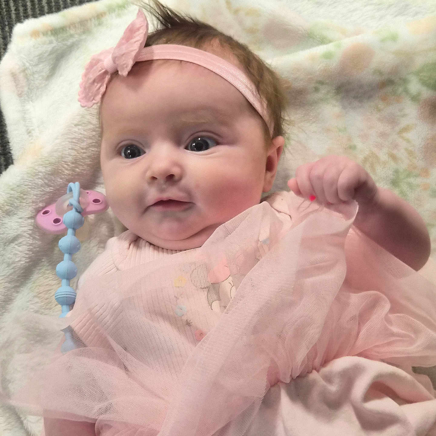Pyper is registered to the contest to win money with this photo: baby, infant, pink_dress, headband, blanket, pacifier_clip, clothing, cute, child, portrait, lying_down, soft_toys, indoors, person, newborn, adorable, happy, small_hand, face, young