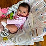 baby, infant, child, smiling, portrait, indoor, bouncer, blanket, toy, stuffed_animal, pacifier, pink_clothing, wooden_floor, play_mat, seated, happy, face, brown_hair, baby_gear, home