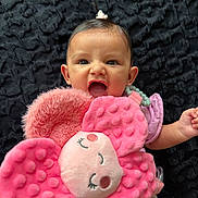 Julietta is registered to the contest to win money with this photo: baby, infant, child, portrait, smiling, surprised, open_mouth, lying_down, plush_toy, stuffed_flower, pink, blanket, dark_background, baby_clothing, headband, bracelet, hand, indoor, close_up, cute
