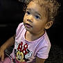 child, toddler, indoor, pink_shirt, minnie_mouse, curly_hair, carpet, cushion, patterned, person, cute, casual_clothing, earring, sitting, looking_up, young_child, curious, small_child, playful, comfortable