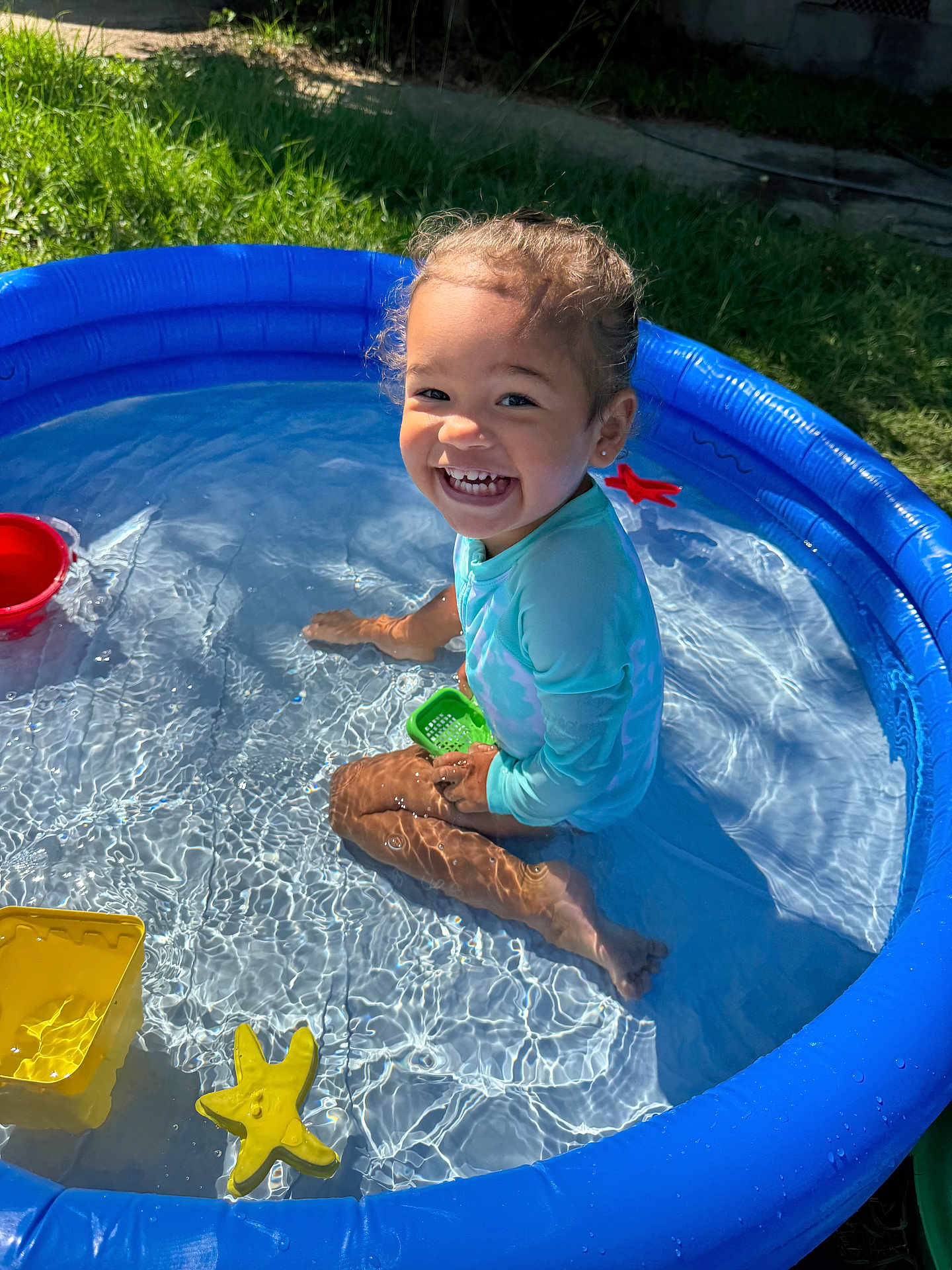 Aniyah is registered to the contest to win money with this photo: child, toddler, pool, water, blue, toy, starfish, bucket, grass, outdoor, sunlight, smiling, happy, sitting, play, summer, fun, plastic, daylight, skin