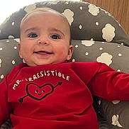 Benjamín joined the competition — help win amazing prizes! baby, smiling, red_sweater, heart_graphic, arrow, cushioned_chair, cloud_pattern, gray, comfortable, happy, child, indoor, portrait, cute, young, infant, clothing, seated, bright, expression