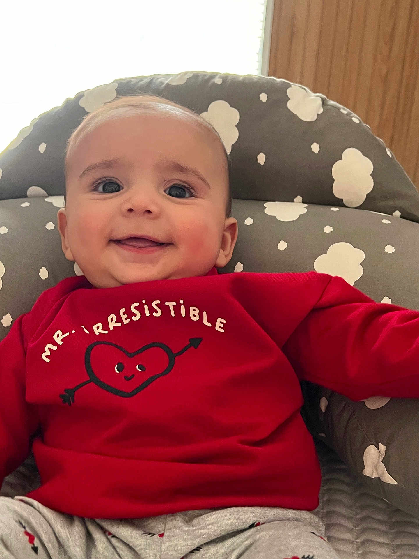 Benjamín joined the competition — help win amazing prizes! baby, smiling, red_sweater, heart_graphic, arrow, cushioned_chair, cloud_pattern, gray, comfortable, happy, child, indoor, portrait, cute, young, infant, clothing, seated, bright, expression