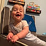 Declan is registered to the contest to win money with this photo: baby, child, smiling, chair, bookshelf, books, nursery, indoor, wall, wooden_letters, blue_blanket, plush_furniture, cute, happy, infant, person, home, decor, light, young_child