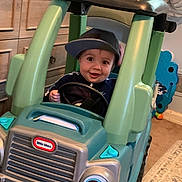 Declan is registered to the contest to win money with this photo: toddler, child, toy_car, little_tikes, cap, indoor, play, smile, face, steering_wheel, car, plastic, furniture, carpet, drawer, happy, hat, room, child_playing, fun