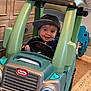 toddler, child, toy_car, little_tikes, cap, indoor, play, smile, face, steering_wheel, car, plastic, furniture, carpet, drawer, happy, hat, room, child_playing, fun