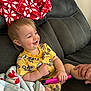 Declan is registered to the contest to win money with this photo: toddler, child, smiling, yellow_clothing, toy, blanket, couch, hand, indoor, happy, face, person, furniture, seated, cute, cozy, playful, comfort, relaxed, home