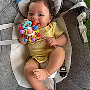 Easton is registered to the contest to win money with this photo: baby, baby_rocker, child, clothing, comfort, curly_hair, cushion, fabric, foot, grass, hand, happy, indoor, infant, person, play, seat_belt, smile, toy, yellow_onesie