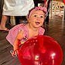 toddler, balloon, red_balloon, child, indoor, wooden_floor, headband, dress, red_dress, happy, smiling, person, floor, legs, white_skirt, sandals, furniture, table, chair, home