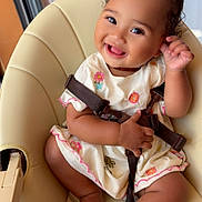Syarah participe au concours pour gagner de l'argent avec cette photo : baby, child, smiling, high_chair, pink_bows, dress, embroidery, happy, cute, indoors, seatbelt, playful, toddler, skin, foot, hand, face, person, furniture, window