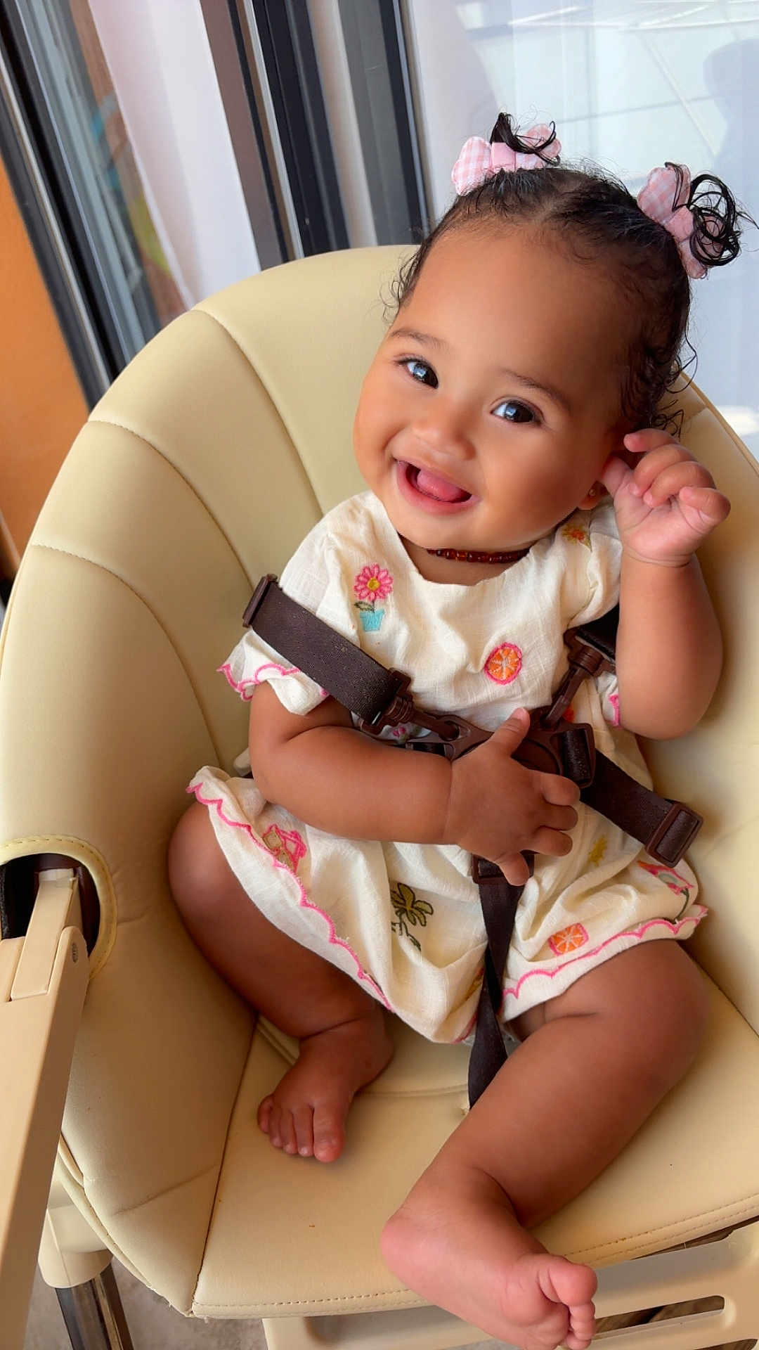 Syarah participe au concours pour gagner de l'argent avec cette photo : baby, child, smiling, high_chair, pink_bows, dress, embroidery, happy, cute, indoors, seatbelt, playful, toddler, skin, foot, hand, face, person, furniture, window