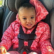Xoe is registered to the contest to win money with this photo: child, toddler, car_seat, pink_jacket, heart_pattern, safety_harness, smiling, happy, indoors, seat_belt, car, sunlight, young_child, cute, portrait, clothing, hair_puff, seat, baby, casual