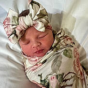 Phebe is registered to the contest to win money with this photo: baby, newborn, sleeping, swaddle, headband, bow, floral_pattern, soft_fabric, close_up, portrait, infant, peaceful, resting, cute, child, wrapped, white_background, face, skin, indoors
