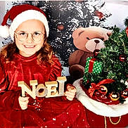 Thalia a rejoint le concours — aidez-le/la à gagner de superbes lots ! child, girl, santa_hat, glasses, red_dress, noel_sign, christmas_tree, presents, teddy_bear, holiday, festive, smile, indoor, celebration, decorations, toy, christmas_balls, red_ribbons, happy, portrait