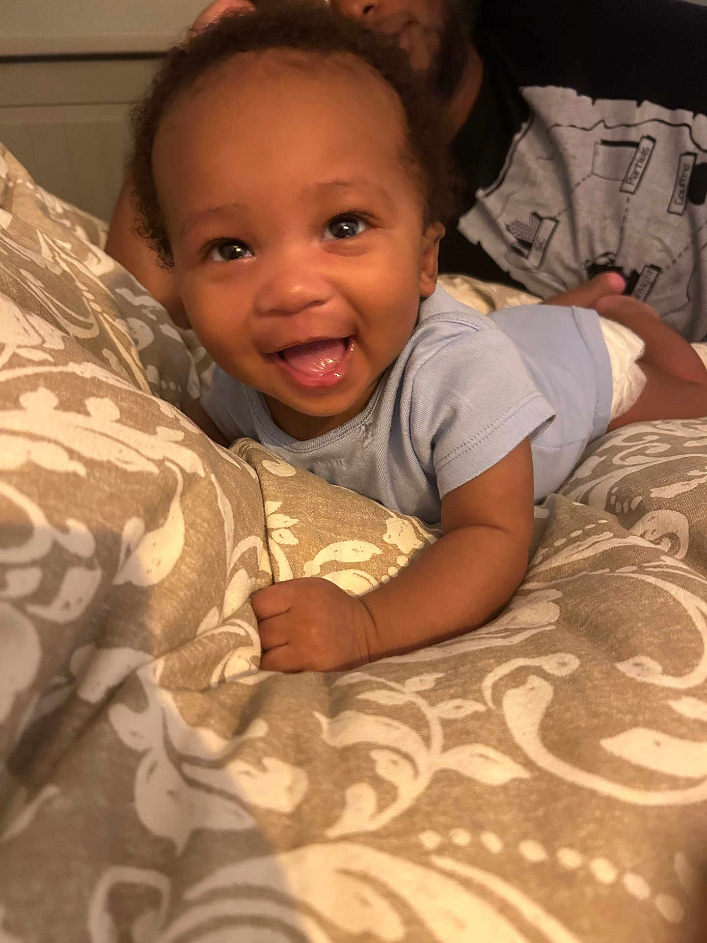 Lyam participe au concours pour gagner de l'argent avec cette photo : baby, smiling, infant, blanket, patterned_blanket, bedroom, person, adult, indoor, happy, cute, child, face, onesie, lying_down, close_up, skin, hand, curly_hair, portrait