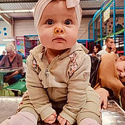 Lola participe au concours pour gagner de l'argent avec cette photo : baby, child, headband, pink, socks, jacket, table, indoor, playground, people, woman, man, seated, curious, face, portrait, clothing, indoor_lighting, expression, casual