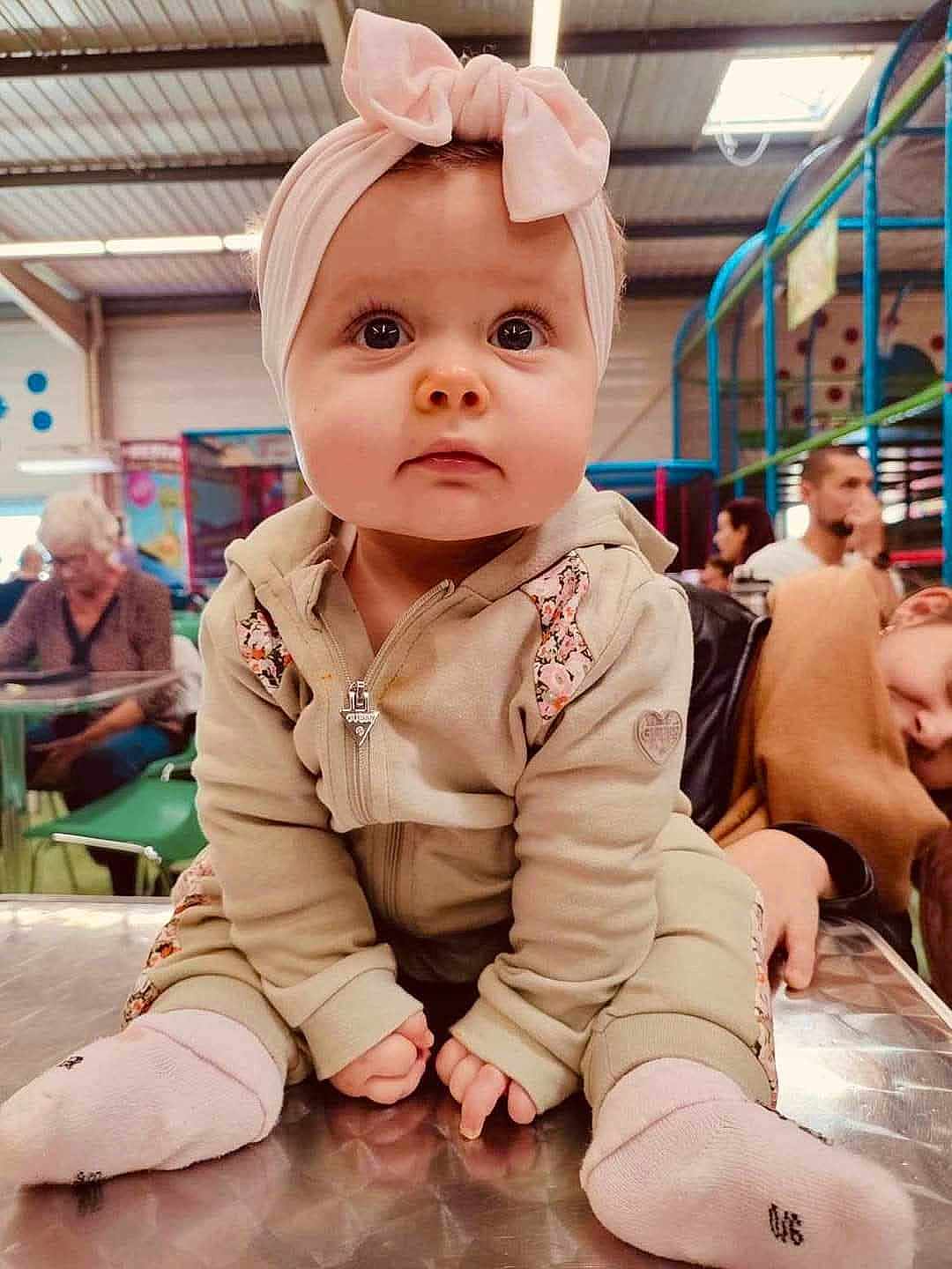 Lola participe au concours pour gagner de l'argent avec cette photo : baby, child, headband, pink, socks, jacket, table, indoor, playground, people, woman, man, seated, curious, face, portrait, clothing, indoor_lighting, expression, casual