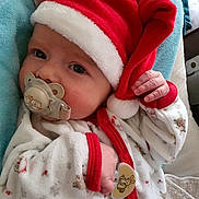 Augustin a rejoint le concours — aidez-le/la à gagner de superbes lots ! baby, pacifier, santa_hat, holiday_pajamas, blanket, infant, cute, sleepy, hand, face, clothing, red_trim, white_fabric, patterned_fabric, indoors, portrait, child, newborn, soft_texture, cozy