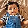 baby, bed, blanket, child, clothing, cute, denim_overalls, face, hair, indoor, infant, laying_down, looking_away, person, portrait, skin, smiling, striped_shirt, toddler, young_child