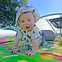 baby, blue_sky, child, crawling, daytime, dinosaur_pattern, grass, greenery, happy, hat, infant, nature, outdoor, person, play_mat, shirt, smiling, sun_hat, sunlight, tree