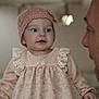 baby, child, infant, dress, knitted_hat, bow, person, face, portrait, curious, cute, soft_lighting, indoor, adult, interaction, closeup, expression, warm, family, clothing