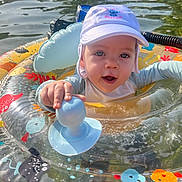 Liam a rejoint le concours — aidez-le/la à gagner de superbes lots ! baby, child, colorful, cute, fish_pattern, float, happy, hat, inflatable_ring, nature, outdoor, playful, recreation, summer, sunlight, swimming, swimwear, toy, water, water_sports