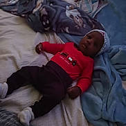 Jeremiah is registered to the contest to win money with this photo: baby, child, bed, blanket, clothing, hat, infant, lying_down, person, red_shirt, socks, soft_fabric, cute, indoors, cozy, portrait, toddler, resting, sleepwear, headwear