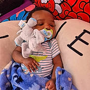 Isiah is registered to the contest to win money with this photo: baby, infant, pacifier, plush_toy, elephant_toy, blanket, blue_blanket, striped_onesie, cushion, hello_kitty, child, indoor, resting, sleepy, soft_toy, comfort, cute, closeup, fabric, hand