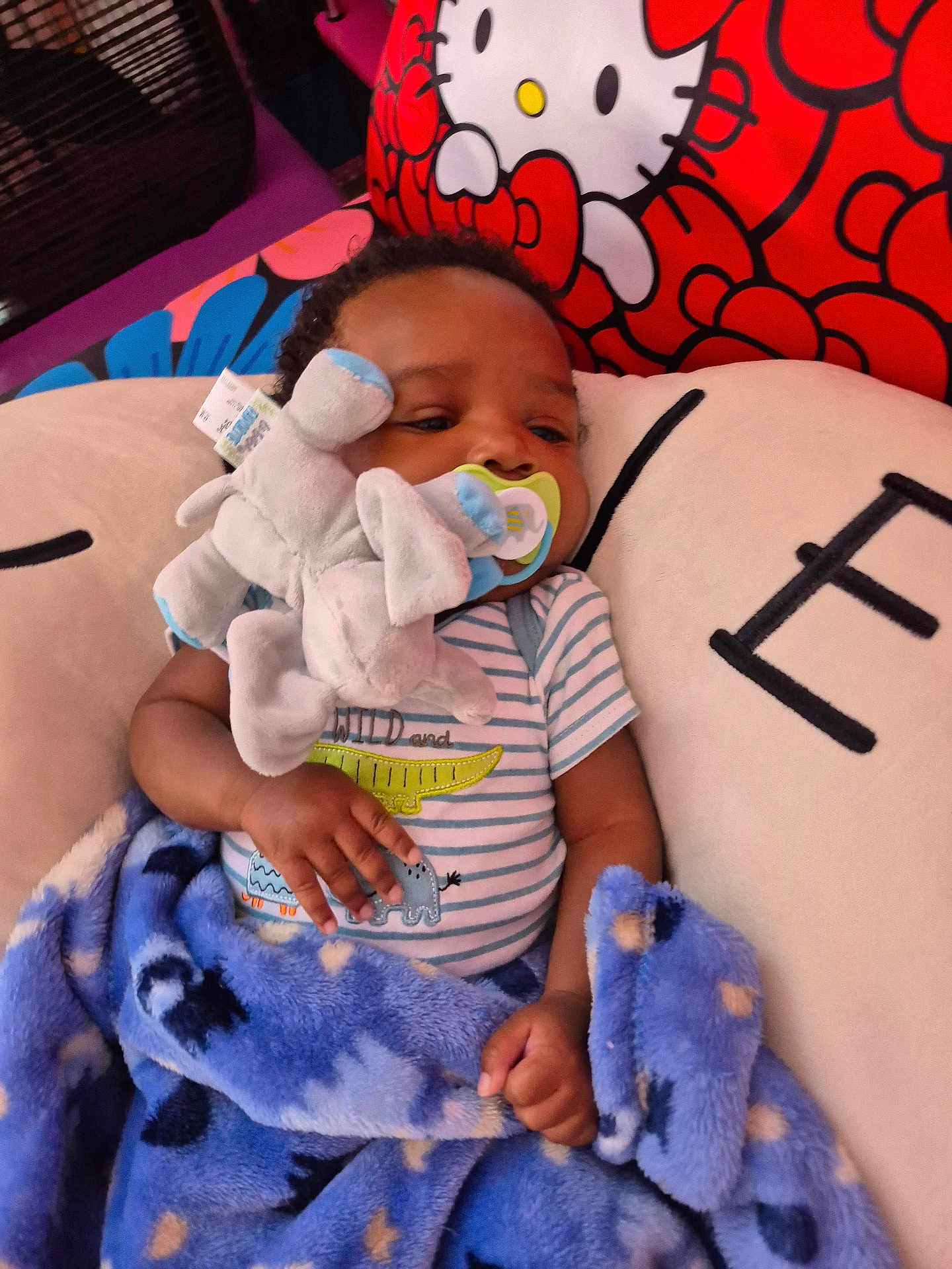Isiah is registered to the contest to win money with this photo: baby, infant, pacifier, plush_toy, elephant_toy, blanket, blue_blanket, striped_onesie, cushion, hello_kitty, child, indoor, resting, sleepy, soft_toy, comfort, cute, closeup, fabric, hand