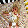 Octavia is registered to the contest to win money with this photo: baby, crib, onesie, hello_kitty, smile, floral_pattern, infant, happy, child, furniture, bed, cute, lying_down, indoors, person, clothing, yellow, white, pink, skin
