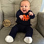 baby, infant, smiling, happy, sitting, chair, armchair, clothing, sweater, pants, dinosaur, orange, navy_blue, white_socks, milestone, wooden_sign, face, person, indoor, cute
