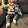 baby, pacifier, sunglasses, jacket, pants, socks, couch, furniture, indoor, child, person, cozy, relaxing, plush, cute, fashion, reflection, headwear, seated, comfortable