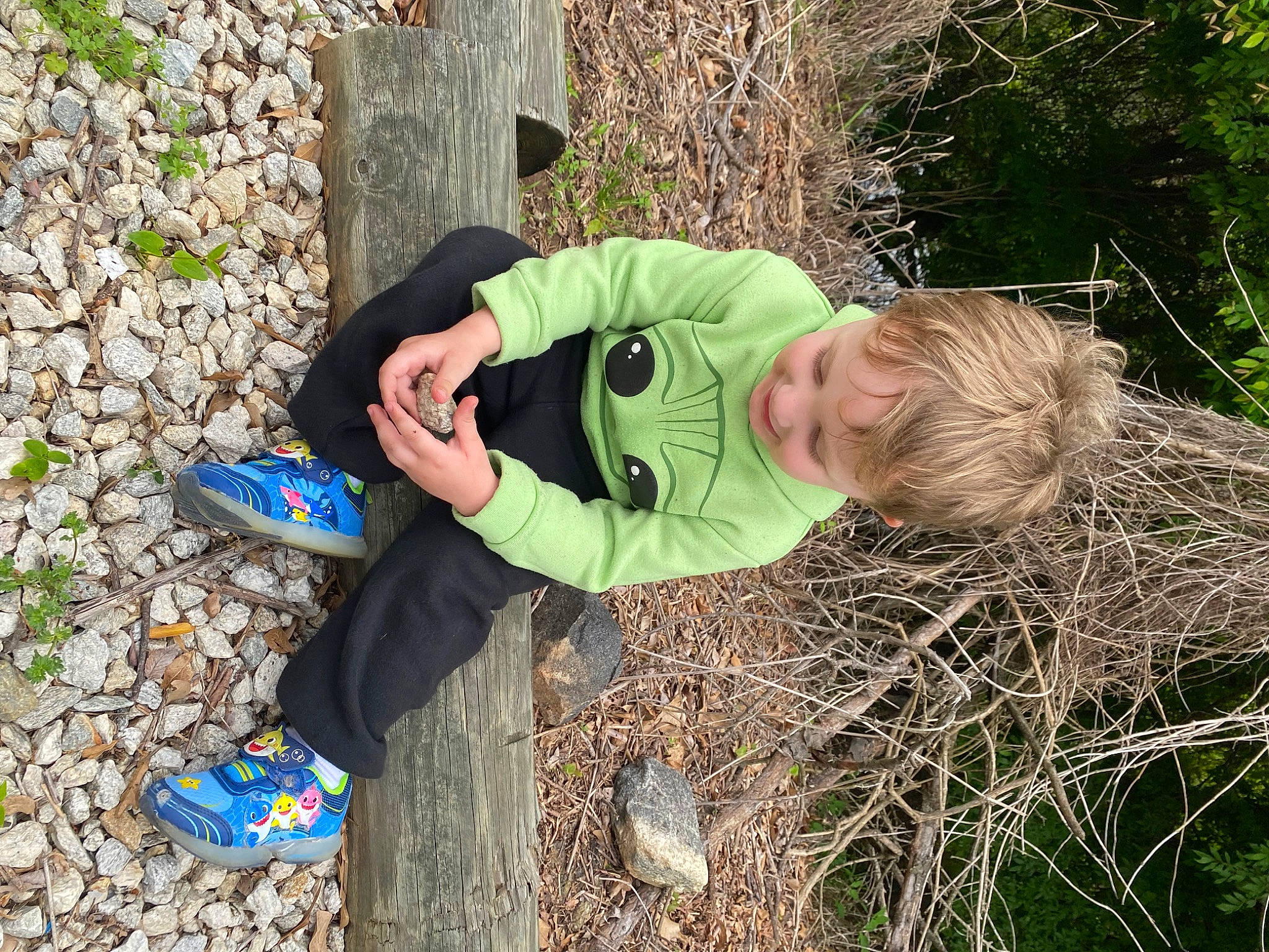 Harlan is registered to the contest to win money with this photo: child, electric_blue, fun, grass, grassland, groundcover, landscape, leisure, outdoor_shoe, people_in_nature, person, plant, recreation, sitting, soil, toddler, tree, trunk, walking_shoe, wood