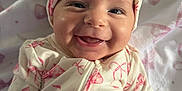 Magnolia is registered to the contest to win money with this photo: baby, infant, smile, smiling, headband, bow, onesie, bow_pattern, blanket, bed, portrait, close_up, cheek, fist, hand, eyes, teething, cute, skin, happy