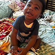 Elleior is registered to the contest to win money with this photo: baby, toddler, child, indoor, bed, blanket, clothing, footwear, curly_hair, person, playing, striped_shorts, blue_shirt, room, messy, soft_toys, hands, looking_up, cute, casual