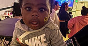 Elleior is registered to the contest to win money with this photo: baby, ceiling, chair, child, conversation, curly_hair, face, floor, group, hand, hoodie, indoor, light, nike, people, person, portrait, smiley_face_sticker, string_lights, table