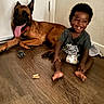 child, toddler, dog, indoor, floor, smiling, happy, pet, animal, baby, canine, tongue_out, wooden_floor, sitting, playful, domestic, friendship, cute, young, casual