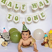 Maverick is registered to the contest to win money with this photo: baby, child, crawling, party_hat, balloons, stuffed_animals, celebration, milestone, banner, smiling, indoor, cute, giraffe, elephant, teddy_bear, white_background, six_months, happy, festive, portrait