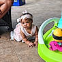 baby, infant, crawling, pink_dress, headband, toy, floor, tile, indoor, child, wicker_chair, curious, serious_expression, cute, hands, feet, person, young_child, colorful, playtime