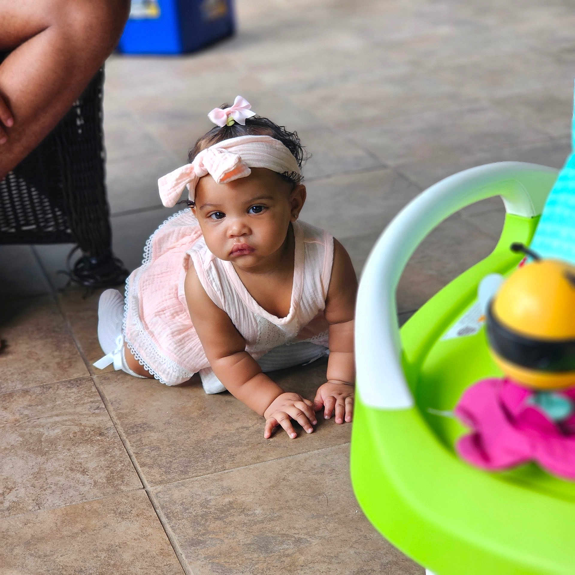 Navanii is registered to the contest to win money with this photo: baby, child, colorful, crawling, curious, cute, feet, floor, hands, headband, indoor, infant, person, pink_dress, playtime, serious_expression, tile, toy, wicker_chair, young_child