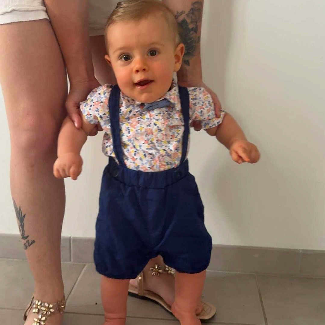 Jules a rejoint le concours — aidez-le/la à gagner de superbes lots ! adult, baby, child, clothing, cute, floor, floral_shirt, hands, indoor, legs, person, sandals, shoes, standing, support, suspenders, tattoo, tiles, toddler, white_wall