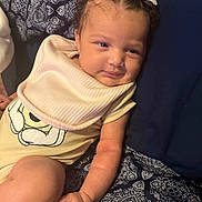 Sarayah is registered to the contest to win money with this photo: arm, baby, bib, clothing, comfort, cushion, cute, face, hand, headband, indoor, infant, pattern, person, portrait, relaxed, seated, skin, smile, young_child