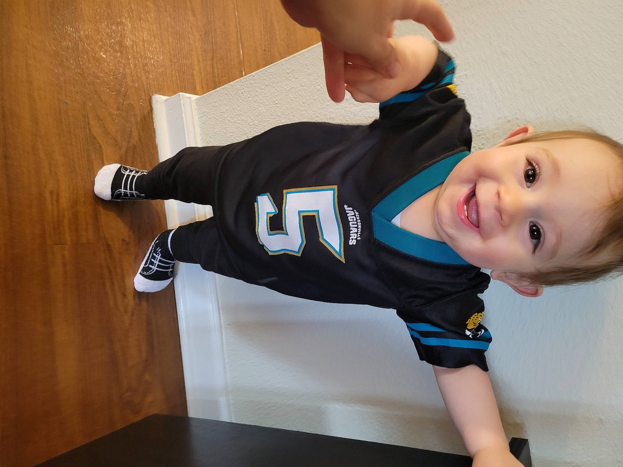 Mikey is registered to the contest to win money with this photo: baby_toddler_clothing, elbow, electric_blue, finger, flooring, gesture, happy, jersey, joint, joy, knee, person, shoulder, sleeve, smile, sports_jersey, sports_uniform, sportswear, t_shirt, thigh