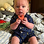 baby, pacifier, romper, banana_pattern, bed, blanket, stuffed_animal, clothing, child, indoor, person, cute, sitting, blue_eyes, infant, soft_toys, curious, skin, hand, portrait
